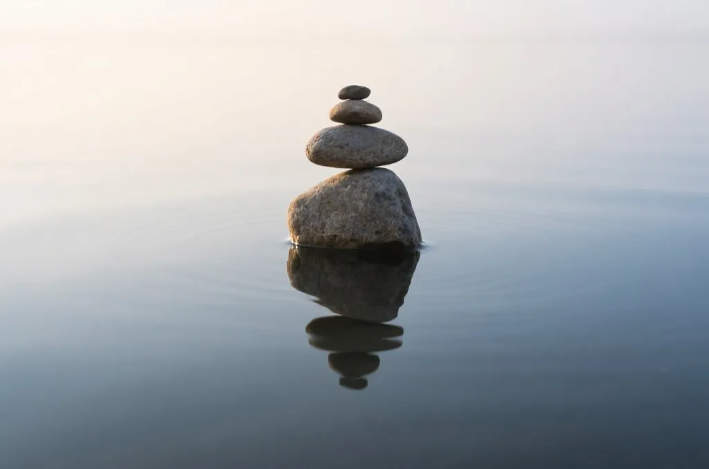 平静水面上堆叠的平衡石，象征平稳的心态和科学的策略管理